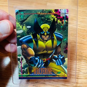 May include: A Wolverine trading card in a clear protective sleeve. The card features a colorful illustration of Wolverine in his classic yellow and blue costume, with the word "Wolverine" at the bottom. The sleeve is labeled "Card Savers II".