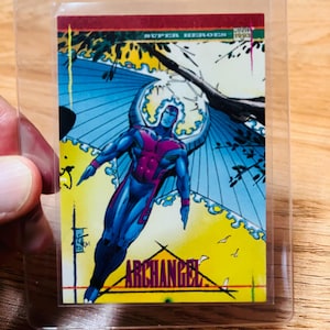 May include: A trading card featuring the Marvel Comics character Archangel, encased in a protective sleeve. The card depicts Archangel in a dynamic pose with blue wings, a red chest, and blue and red suit. The card has the text "ARCHANGEL" and "SUPER HEROES".