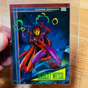 May include: A trading card featuring the Scarlet Witch from the Super Heroes series. The card shows a comic book illustration of the character in a dynamic pose, with a red and purple costume, against a starry background. The card is encased in a protective sleeve.