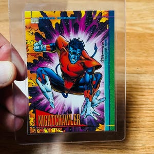 May include: A Nightcrawler trading card from the Marvel Super Heroes series, featuring the character in a dynamic pose. The card has a vibrant design with a purple and yellow background, and the character is wearing a red and blue costume. The card is in a protective sleeve.