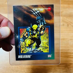 May include: A Wolverine trading card from the Marvel Super Heroes series, encased in a protective sleeve. The card features a dynamic illustration of Wolverine with his claws extended, set against a cosmic background. The card is from 1992.