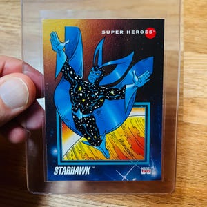May include: A Starhawk trading card from the Super Heroes series, featuring a cosmic character in blue and black with a starry pattern. The card is in a protective sleeve, with the Marvel 1992 logo.