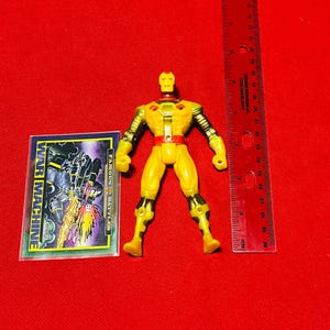 May include: Yellow and black action figure of War Machine from the Marvel Comics universe. The figure is posed standing with its arms outstretched. The figure is approximately 4 inches tall. The figure is packaged with a card featuring a comic book image of War Machine.