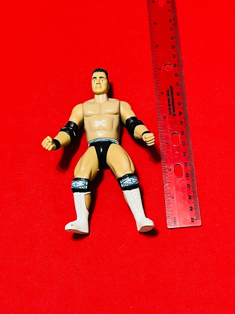 May include: A wrestling action figure with black and white details. The figure is posed with arms raised and fists clenched. The figure is standing on a red surface.