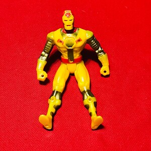 May include: Yellow and black action figure of a superhero with a red and yellow helmet. The figure has a black belt and is standing on a red background.