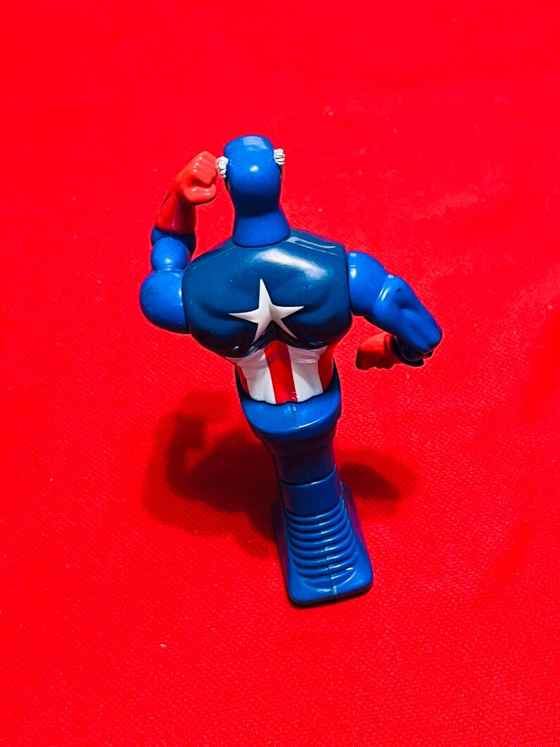 May include: A blue and red plastic action figure of Captain America standing with his arm raised. The figure is wearing a blue and red costume with a white star on the chest.