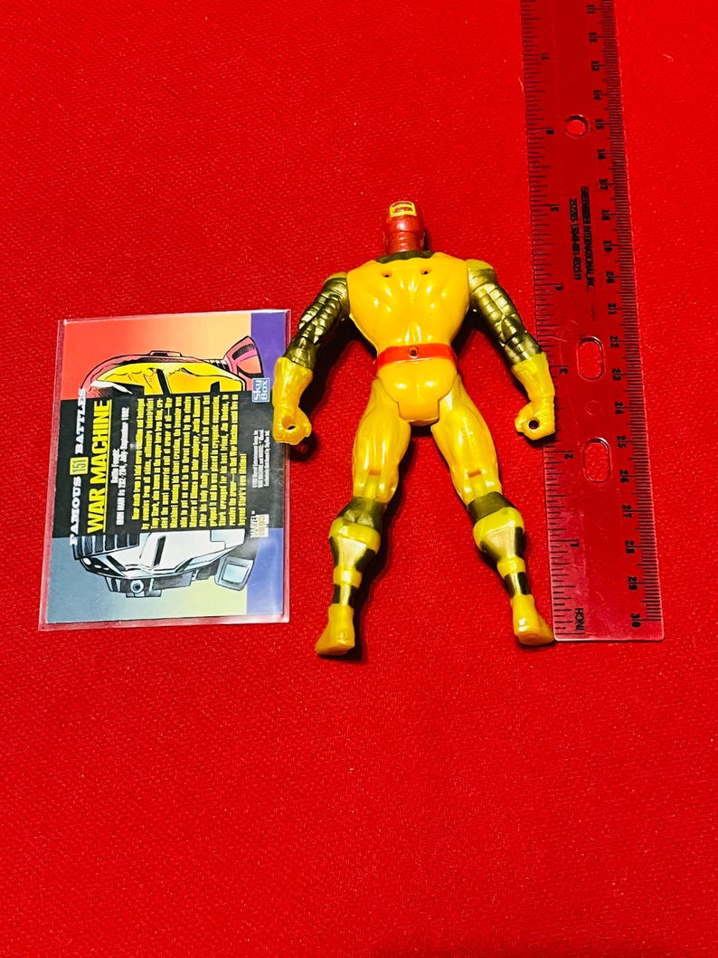 May include: Yellow and red plastic action figure of War Machine from the Marvel Comics universe. The figure is approximately 6 inches tall and has a card with information about the character.
