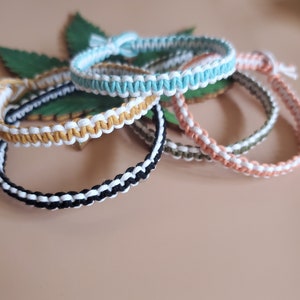 May include: Five colorful friendship bracelets made of woven string. The bracelets are in shades of black, white, yellow, green, and light blue.