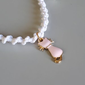 May include: White crocheted bracelet with a pink cat charm. The cat charm has gold accents and a shiny finish.