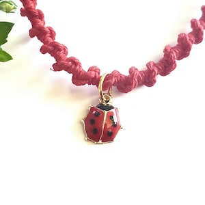 May include: Red string bracelet with a gold ladybug charm. The ladybug has black spots and a black head.