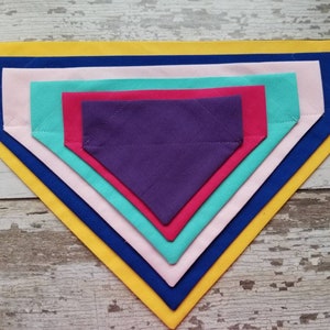 May include: A set of six fabric dog bandanas in various colors, including yellow, blue, pink, red, teal, and purple. The bandanas are layered on top of each other, with the largest bandana on the bottom and the smallest bandana on top.