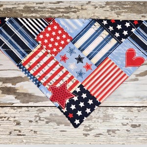 May include: A patriotic dog bandana with a patchwork design. The bandana features various patterns, including red stars on a white background, red and white stripes, and blue stripes. A red heart and star are also included.