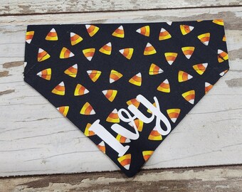 May include: Black and orange candy corn patterned dog bandana with the name "Ivy" in white text.