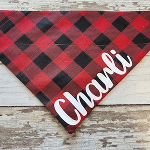 May include: Red and black buffalo plaid dog bandana with the name "Charlie" written in white cursive.