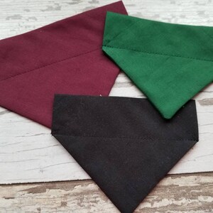 May include: Three fabric dog bandanas in burgundy, black, and green. The bandanas are triangular in shape and have a stitched edge.