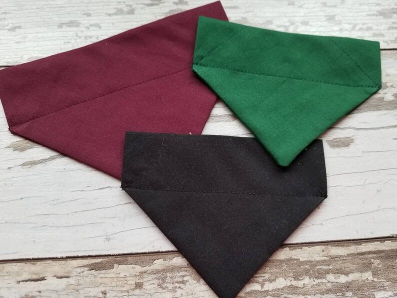 May include: Three fabric dog bandanas in burgundy, black, and green. The bandanas are triangular in shape and have a stitched edge.