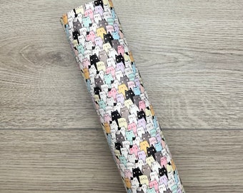 May include: A rolled sheet of patterned fabric featuring a repeating design of cartoon cats in various colors, including black, gray, pink, and yellow. The cats are set against a white background.