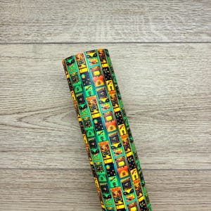May include: A roll of faux leather fabric featuring a repeating pattern of colorful vintage arcade game cabinets. The design includes bright yellow, orange, and green machines set against a dark background, arranged in vertical columns across the material.
