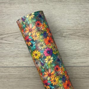 May include: A colorful floral pattern on a fabric roll. The pattern features a variety of flowers in shades of red, orange, yellow, pink, blue, and green. The flowers are outlined in black and have a watercolor effect.