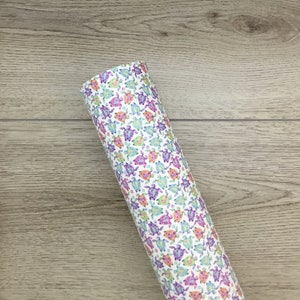 May include: Rolled white fabric with a repeating pattern of colorful sea turtles in shades of purple, blue, orange, and green. The turtles are scattered across the surface of the fabric.