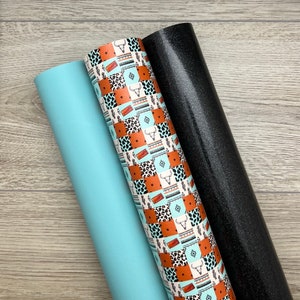 May include: Three rolls of faux leather material. One is a solid light blue, another features a patchwork design with cow skulls, cacti, and geometric patterns in brown, white, and turquoise. The third roll is black with glitter.