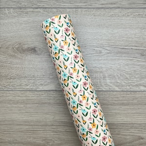 Peut inclure: Un rouleau de papier d'emballage de couleur crème avec un motif floral composé de fleurs bleues, roses, jaunes et vertes. Les fleurs sont disposées en rangées verticales avec des feuilles vertes.