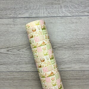 May include: Rolled Easter-themed patterned paper. The design features a patchwork of squares with bunnies, floral baskets, and checkered patterns in pastel pink, green, and beige. The paper is rolled up, showcasing the repeating pattern.