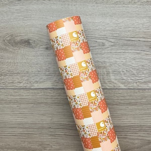 May include: A rolled fabric sheet with a patchwork design. The pattern includes squares of floral, gingham, and dotted prints in peach, orange, and cream. The Carhartt logo is printed on several squares.