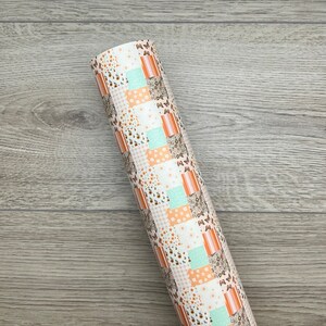 May include: A roll of white vinyl with a patchwork pattern featuring orange, brown, and light blue squares with various floral and geometric designs.