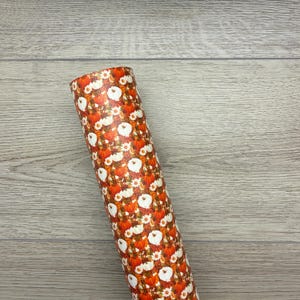 May include: A rolled sheet of material with a repeating pattern of orange pumpkins, white daisies, and brown leaves. The background is a light brown color.