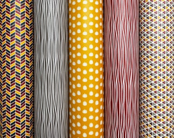May include: Four rolls of patterned fabric in various fall colors. The patterns include a chevron pattern in red, yellow, and black, a wavy line pattern in black and white, a pumpkin pattern in white and yellow, and a triangle pattern in red, yellow, green, and black.