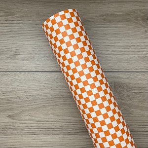 May include: Rolled sheet of orange and white checkered faux leather. The pattern is a classic checkerboard design, with alternating squares of orange and white. The material is rolled up, showing the pattern on the outside.