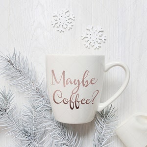 Pu&ograve; includere: Tazza da caff&egrave; in ceramica bianca con il testo "Maybe Coffee?" in lettere rosa oro. La tazza &egrave; circondata da rami di pino bianchi e fiocchi di neve bianchi.