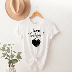 Pu&ograve; includere: Maglietta bianca con testo nero che dice "Love Coffee!" e un grafico a forma di cuore nero.