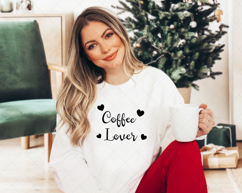Pu&ograve; includere: Una felpa bianca con la scritta "Coffee Lover" in lettere nere e piccoli cuori neri. La modella indossa la felpa e tiene in mano una tazza bianca.