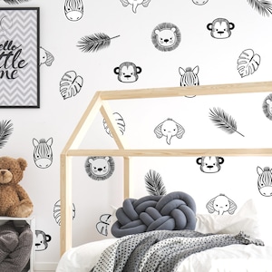 K&ouml;nnte beinhalten: Schwarz-wei&szlig;e Tier- und Blatt-Wandaufkleber an einer wei&szlig;en Wand in einem Kinderzimmer. Die Aufkleber zeigen ein Zebra, einen L&ouml;wen, einen Affen, einen Elefanten und Palmbl&auml;tter.