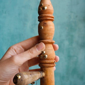 Puede incluir: Un instrumento musical de madera con un cuello largo y delgado y una cabeza redonda y bulbosa. El cuello est&aacute; decorado con detalles met&aacute;licos de color dorado. El instrumento se sostiene en una mano.