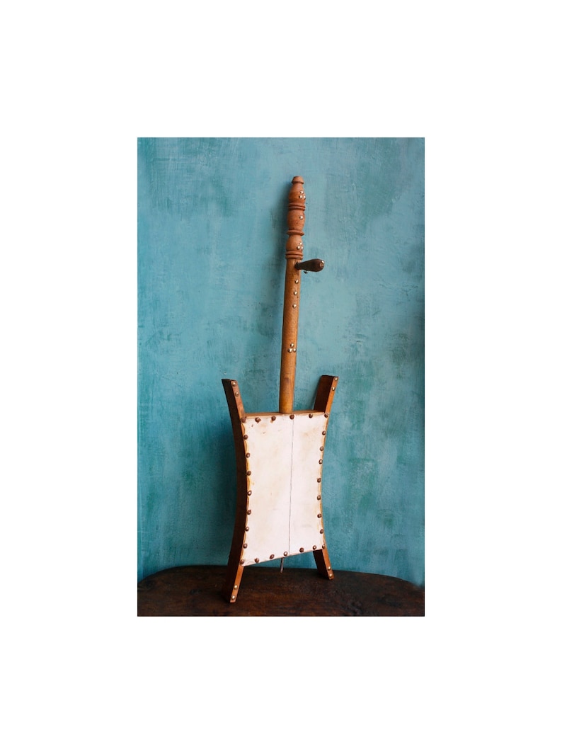 Puede incluir: Un instrumento musical de madera con un cuerpo de cuero blanco y un largo cuello de madera. El instrumento est&aacute; decorado con peque&ntilde;os remaches de metal.