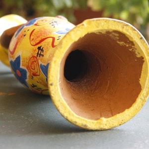 May include: A yellow ceramic vase with a painted design of red, blue, and orange flowers. The vase has a wide opening and a brown interior.