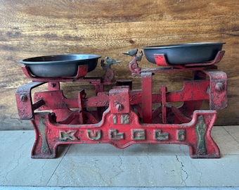May include: Red vintage scale with two black metal bowls. The scale has a 1 kg weight indicator and the word "KULLE" written on the base.