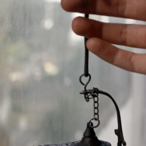 Puede incluir: Una peque&ntilde;a l&aacute;mpara de bronce de estilo antiguo con un pico curvo y un asa decorativa. La l&aacute;mpara est&aacute; suspendida por una cadena y un gancho. El dise&ntilde;o de la l&aacute;mpara recuerda a una l&aacute;mpara de genio.