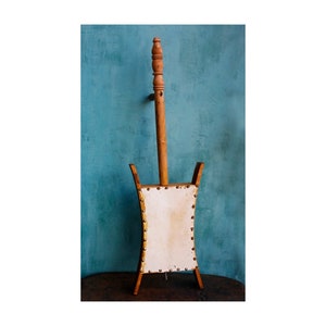 Puede incluir: Un instrumento musical de madera con una caja de resonancia de cuero blanco y un mango de madera. El instrumento est&aacute; decorado con tachuelas de lat&oacute;n.