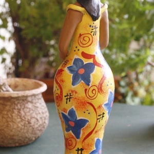 May include: A yellow ceramic figurine of a person wearing a yellow hat with red and black accents. The figurine is painted with blue and red flowers and swirls.