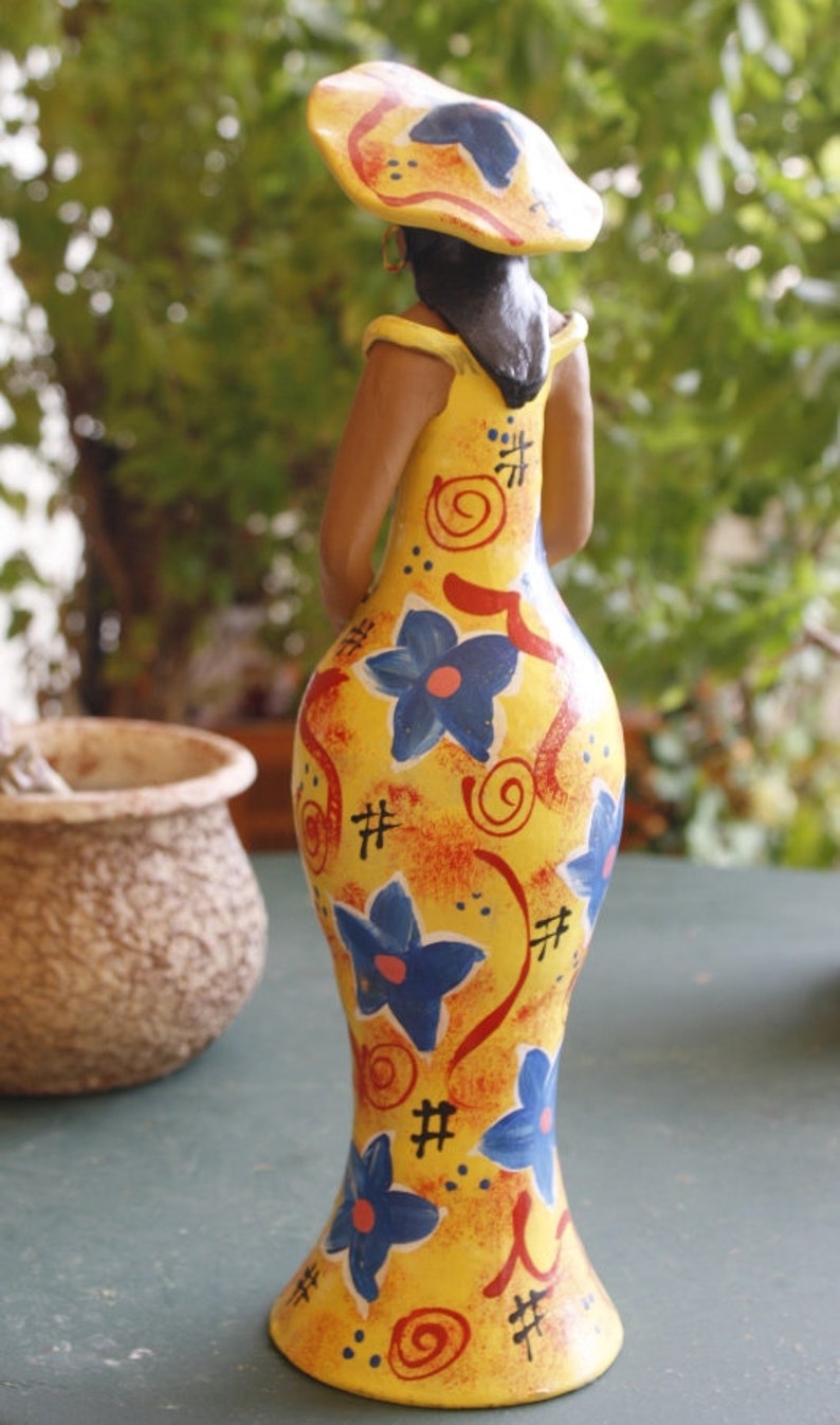 May include: A yellow ceramic figurine of a person wearing a yellow hat with red and black accents. The figurine is painted with blue and red flowers and swirls.