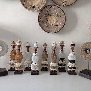 Peut inclure: Une rangée de huit figurines en perles avec des vêtements de couleurs et de motifs différents. Les figurines sont posées sur des socles en bois et sont disposées en ligne. Il y a deux anneaux en perles sur des supports derrière les figurines.