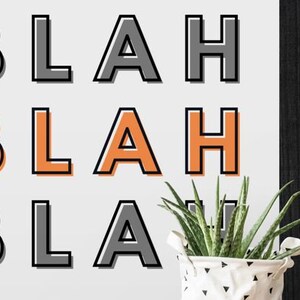May include: A white framed print with the word "BLAH" repeated three times in black and orange lettering.