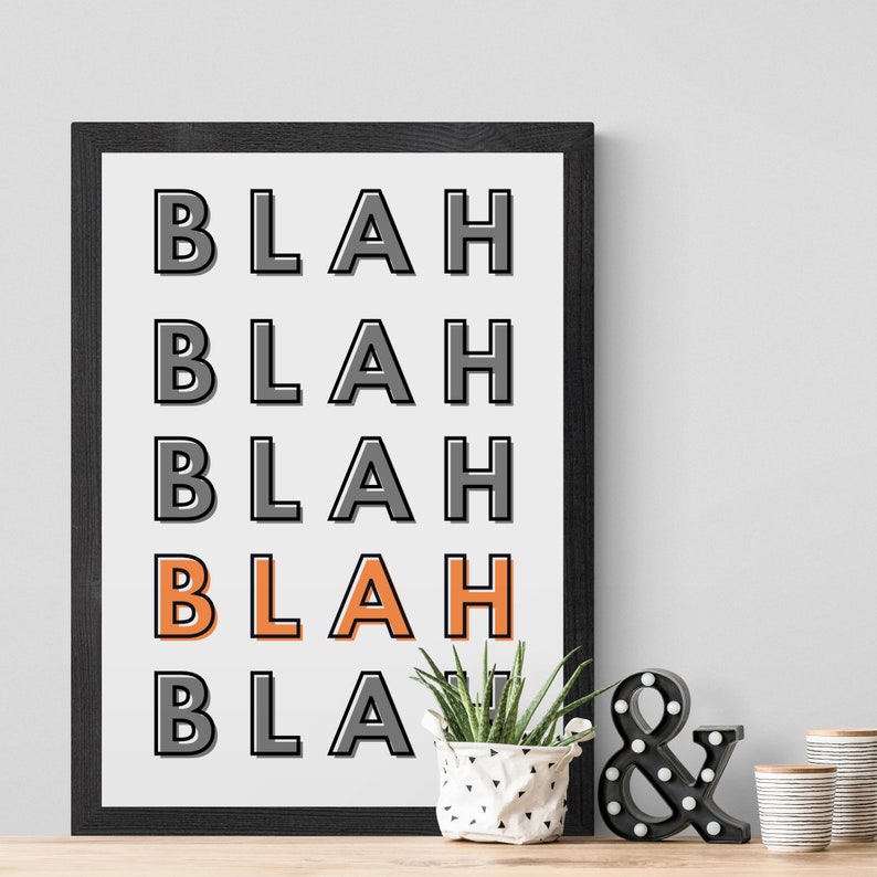 May include: Black framed print with the word "BLAH" repeated five times in a vertical column. The fourth "BLAH" is in orange. A small potted plant and a black light-up ampersand sign are in front of the print.