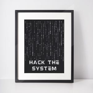 May include: A framed print with a black frame and white mount. The artwork features a black background with a matrix of falling binary code in white. The words "HACK THE SYSTEM" are displayed in white, stylized text.