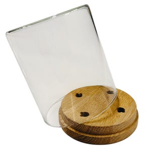 May include: A clear glass cloche with a wooden base. The base is made of two round wooden pieces, with three small holes in the top piece. The glass cloche is tilted, revealing the wooden base.