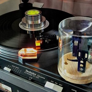 May include: A black Technics Quartz SL-5310 turntable with a record in place. The turntable features a clear protective cover and a wooden base. The controls are visible, and the overall aesthetic is vintage.